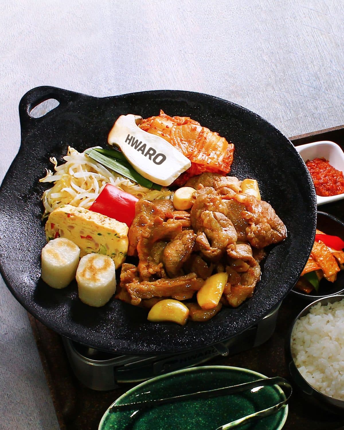 Dwaeji bulgogi searing on the Hwaro griddle with garlic, kimchi and rice cake