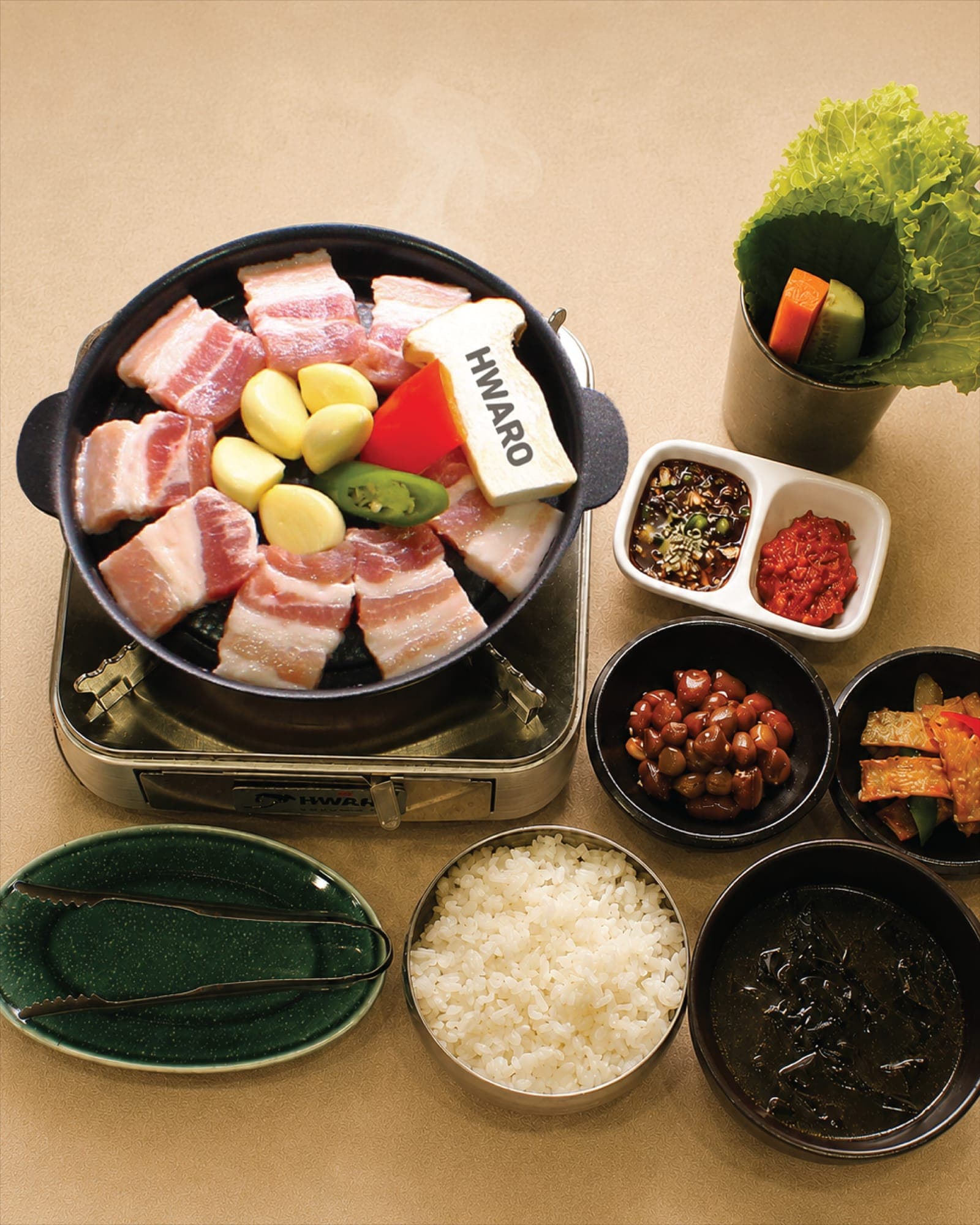Samgyeopsal laid out on the Hwaro griddle with rice, seaweed soup and banchan