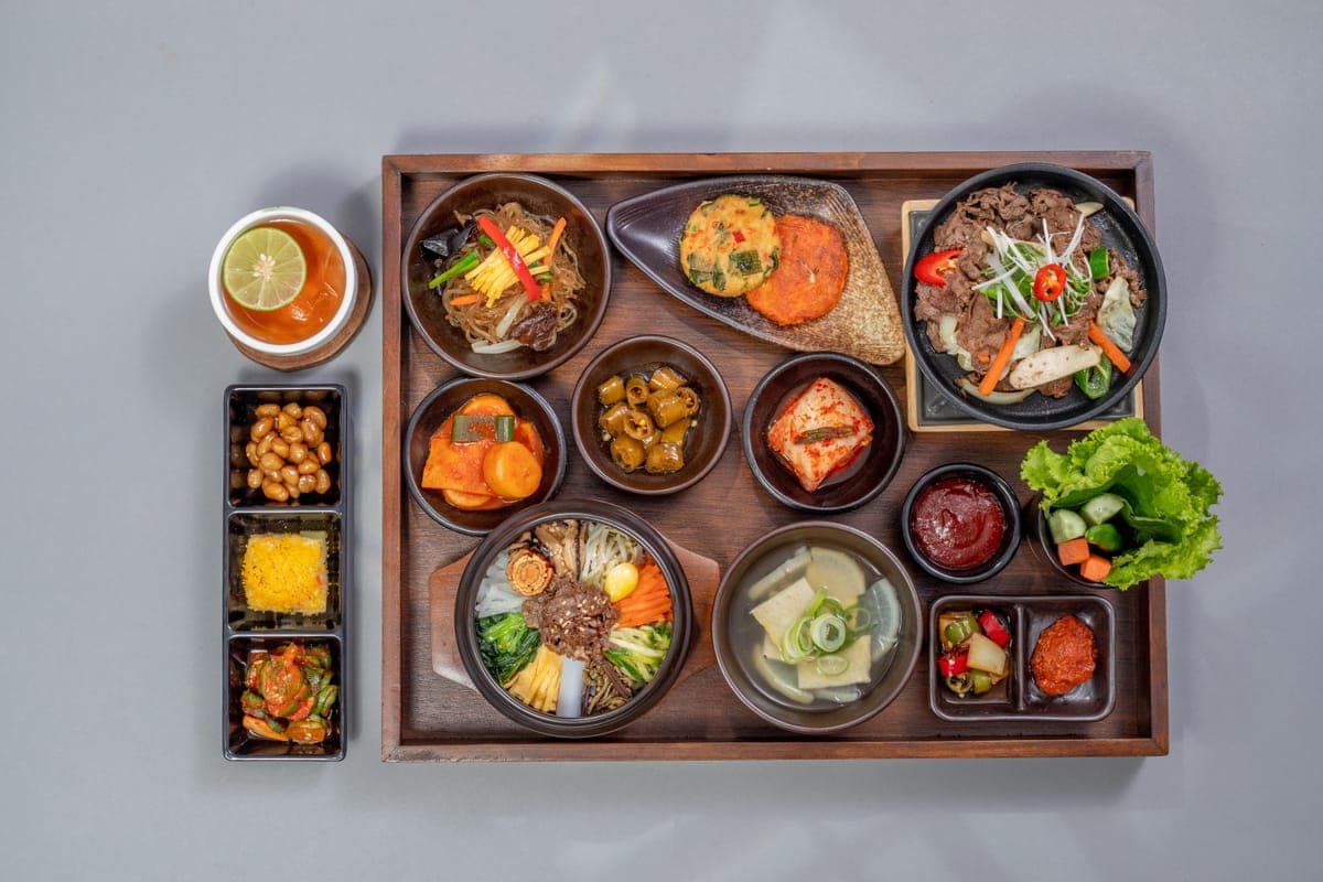 A full Korean tray from above: bibimbap, soup, jeon, japchae and banchan