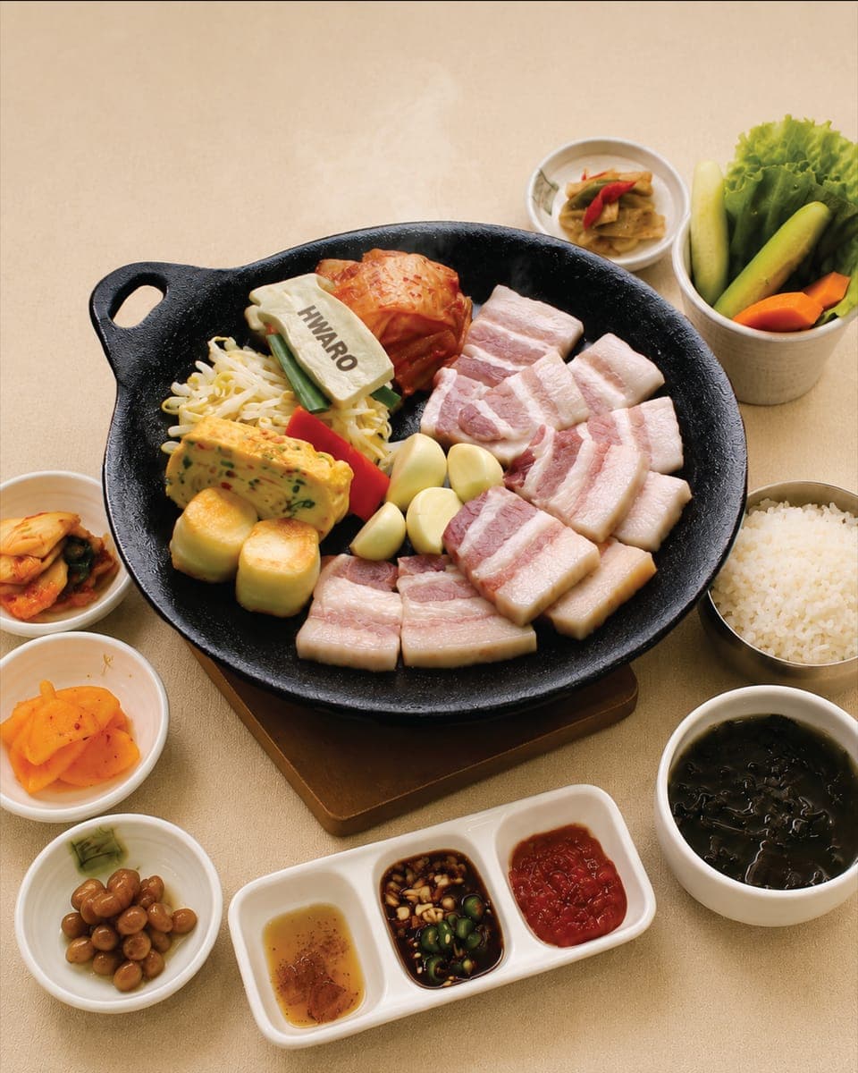 Samgyeopsal, kimchi and rice cake laid out on the Hwaro griddle